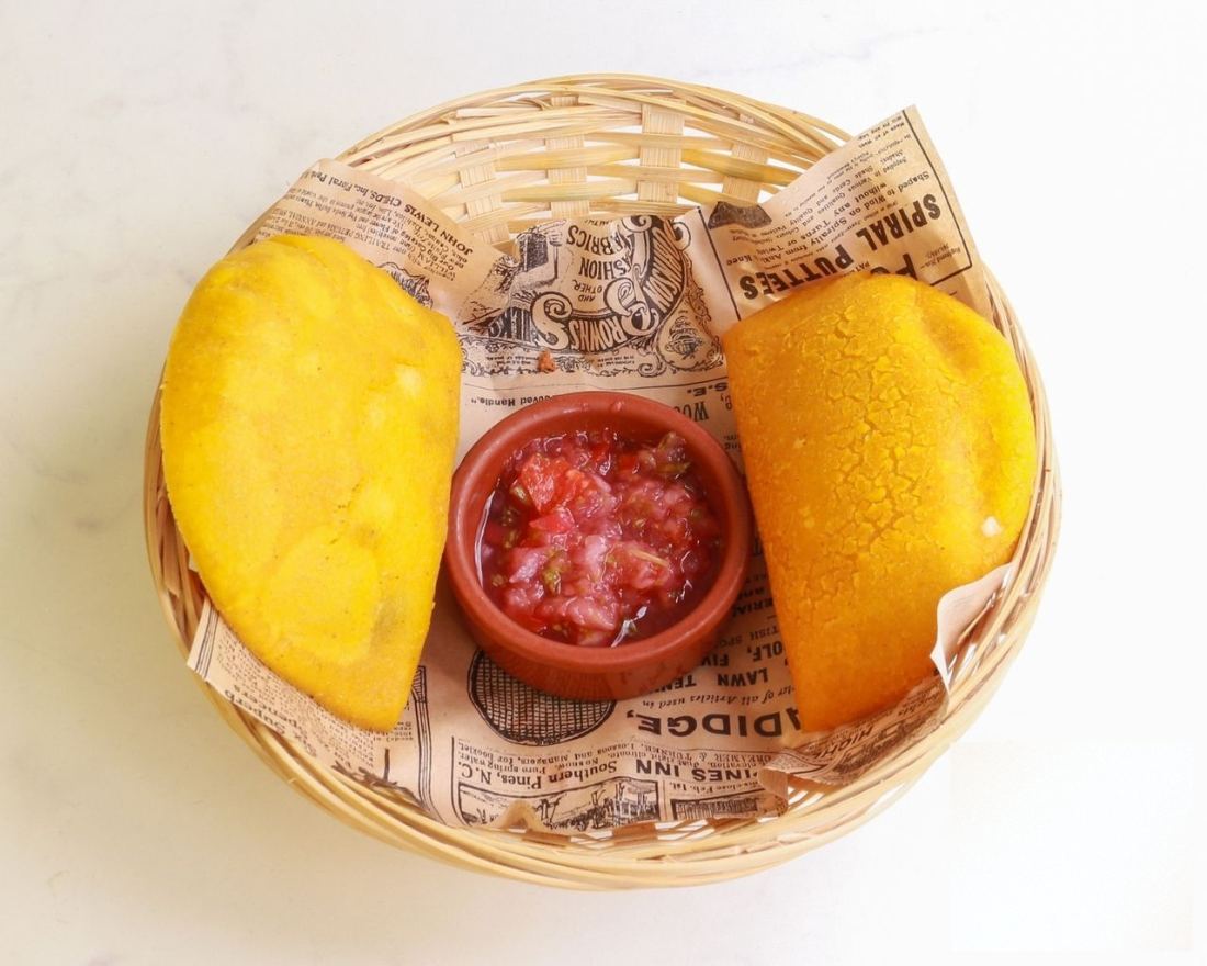 Deux empanadas à la pâte de maïs dorée, servies en panier avec une cassolette de pico de gallo.