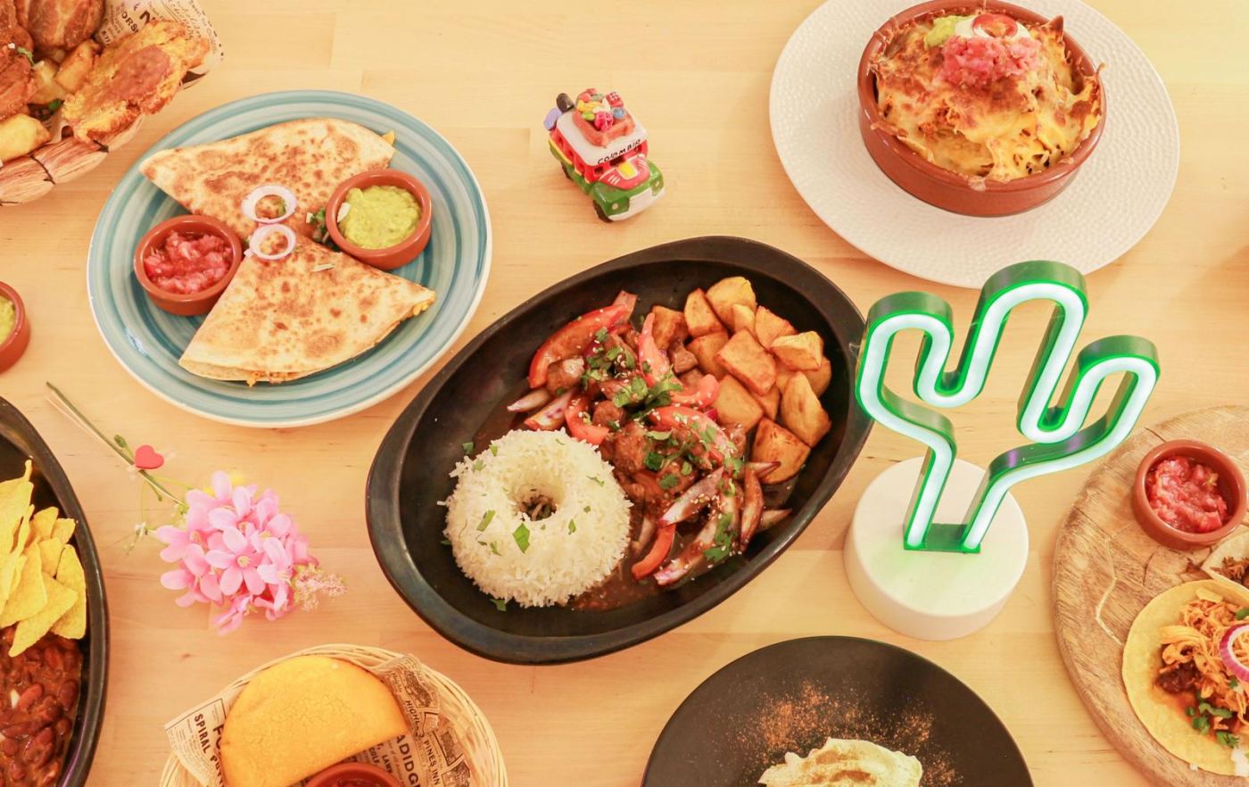 Une grande tablée dressée au Barrio Latino : quesadillas, lomo saltado, nachotes, empanadas, tacos et chicharrón disposés sur une table en bois clair.