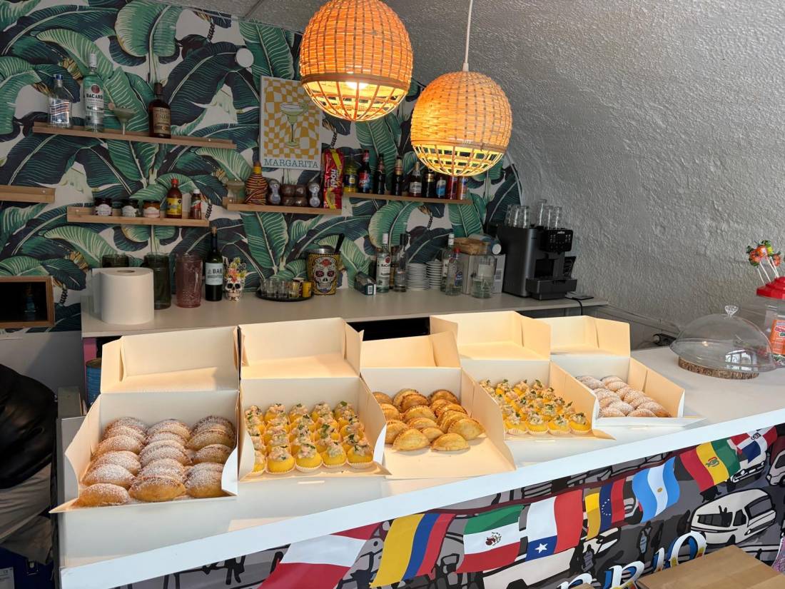 Cinq cartons traiteur remplis d’empanadas, de causas et de chaussons, prêts au départ sur le comptoir du bar du restaurant.