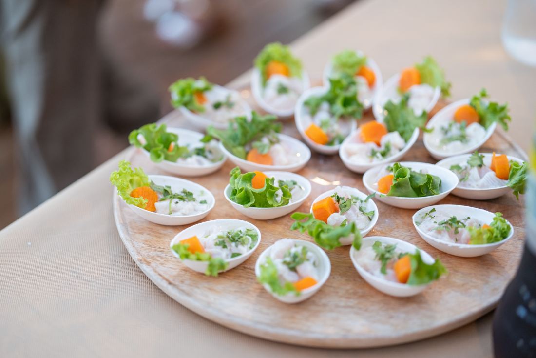 Une planche en bois couverte de verrines de ceviche, garnies de coriandre, de salade et de dés de camote.