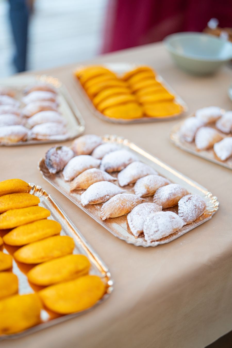 Plateaux d’empanadas alignées : pâte de maïs dorée d’un côté, chaussons sucrés saupoudrés de sucre glace de l’autre.